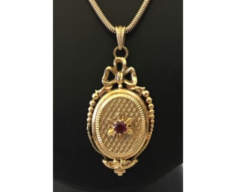 A 9ct gold locket set with a single ruby and bow decoration to top, on a snake chain. Approx. 20.4g. Import hallmarks. Chain 