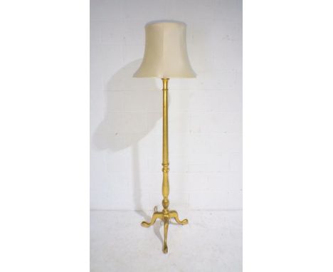 A gilt standard lamp on tripod base with shade.