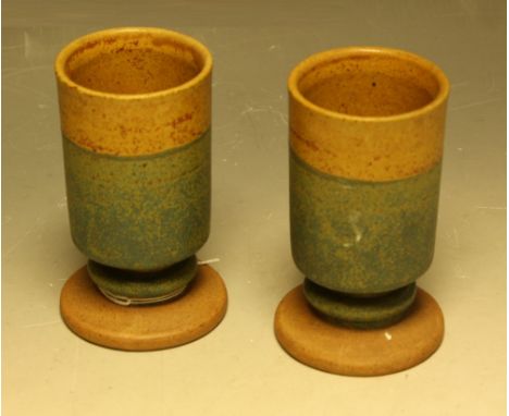 A pair of stoneware cylindrical toasting beakers, by Robin Welch Pottery, glazed in bands of ochre and green, spreading circu