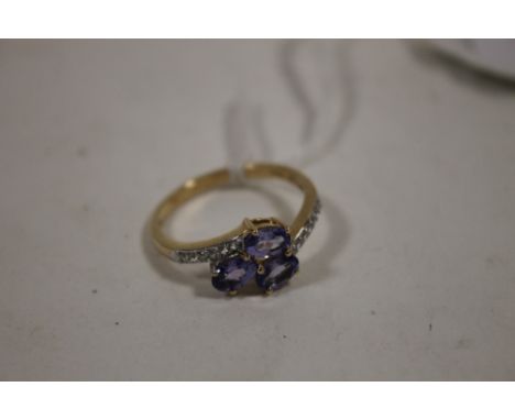 A HALLMARKED 9K GOLD THREE STONE TANZANITE RING, set with three oval tanzanites on a split band set with six white stones eit