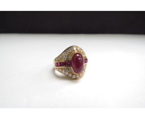 An 18ct gold ring centrally set with a cabochon ruby flanked by a row of square cut rubies all framed with brilliant cut diam