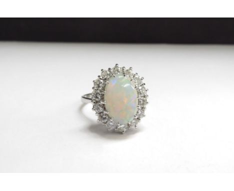 An 18ct white gold opal and diamond cluster ring the centre oval opal 14mm x 9mm framed by 14 brilliant cut diamonds. Size R,