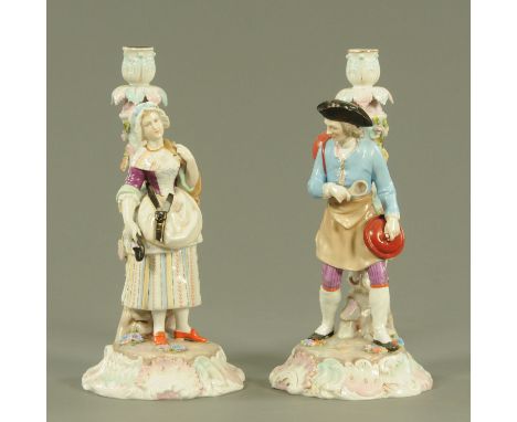 A pair of Continental porcelain figural candlesticks, late 19th century, modelled as male and female merchants on floral encr