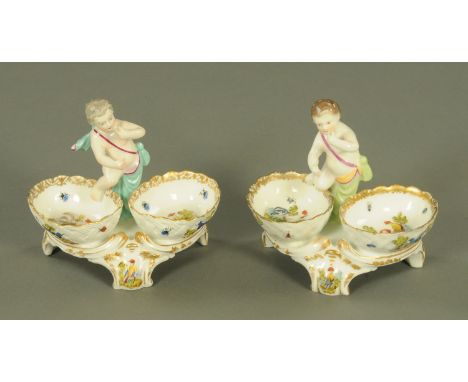 A pair of Samson of Paris porcelain salts, each surmounted with a putti above two oval wells decorated with wildfowl and exot