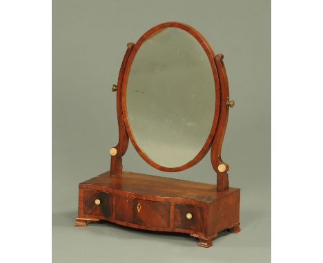 A Georgian mahogany serpentine fronted toilet mirror, the oval glass and shaped supports above a serpentine base with three d