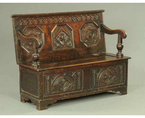 An 18th century carved oak box settle, the three panel back with later Victorian face mask carvings, with shaped arm rests up
