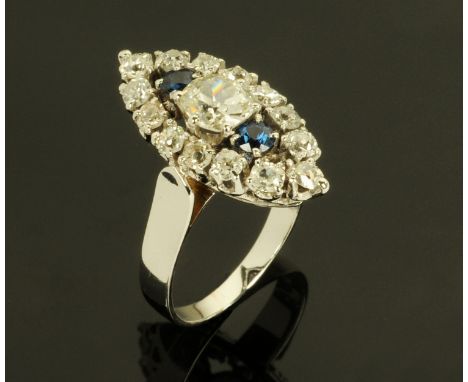A sapphire and diamond boat shaped ring, with large central diamond between two sapphires framed by 14 diamonds on white meta