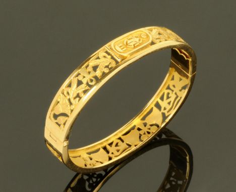An Egyptian gold metal hinged bangle, decorated with a scarab beetle, ankh's, palmettes and the eye of Osiris, struck with Eg