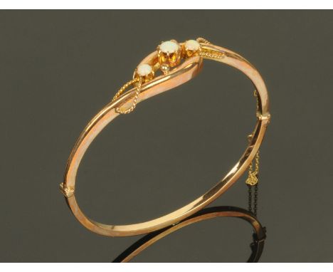 A 9 ct gold hinged bangle set with three opals, interior diameter 6 cm, in original plush fitted and lined case.