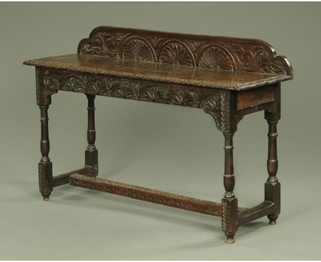 An antique oak side table, converted from a gate leg table and with rear upstand, carved frieze and raised on turned with str