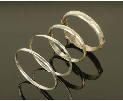 Four silver bangles, two hinged with engraved decoration. CONDITION REPORT: The large foliate bangle has English hallmarks an
