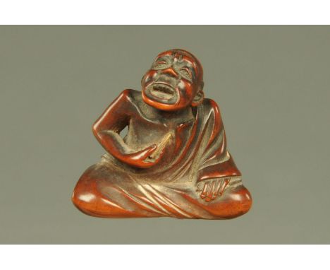 A small Japanese carved hardwood Netsuke, carved as a seated or cross legged man howling in pain as he holds an implement to 
