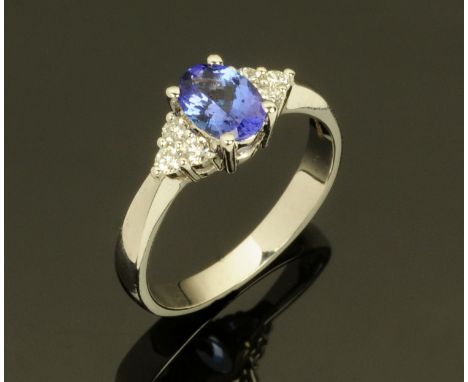 An 18 ct white gold ring set with an oval tanzanite with trefoil of diamonds to each shoulder, total weight +/- 1 carat (see 