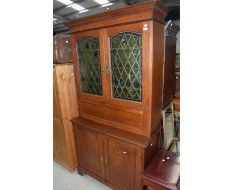 A traditional golden secretaire bureau bookcase in the Arts and Crafts style, having coloured and leaded glass door of convex