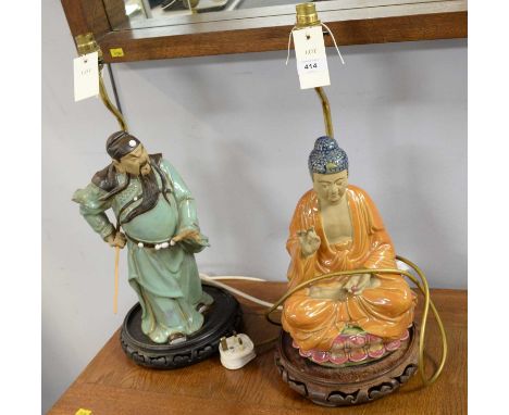 Two Chinese figural table lamps, each with brass light fixture, raised over a pierced stained wood circular base mounted with