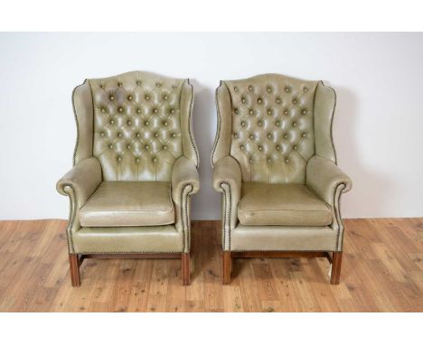A pair of 20th Century wingback armchairs upholstered in light green leatherette, the buttoned backrest flanked by shaped hea