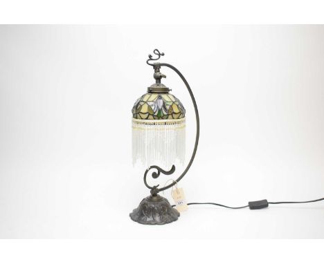 A Tiffany-style table lamp, the stained leaded glass style shade with beaded tassels, raised on a scrolling curved support, t