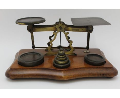 A MECHANICAL POSTAL SCALE, brass construction upon a polished mahogany serpentine shape base, 26cm wide, with weights 