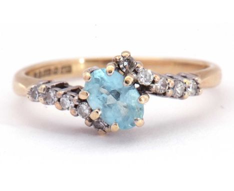 Modern 9ct gold aquamarine and diamond cross-over ring, the oval faceted aquamarine offset and raised between small diamond s