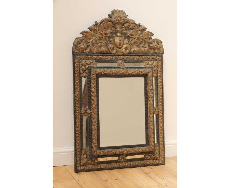An ebonised and embossed brass wall mirror, 19th/20th century, Dutch, the shaped crest decorated with scrolling foliage, over