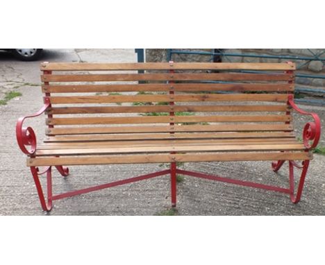 A wrought iron framed garden bench, red painted metal with scroll arms and back detail, with teak slats, 81cm wide, 87cm high