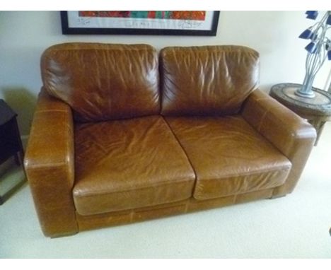 A distressed tan leather upholstered two-piece suite, comprising a deep seated two-person sofa, and a single deep seated armc
