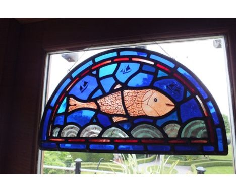 A pair of Paul Eliot stained leaded glass arch topped panels, depicting fish with ships on a blue ground, above waves, signed