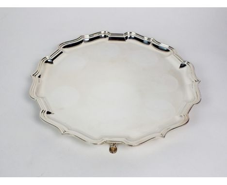 A silver salver, Roberts & Belk, Sheffield 1987, of shaped circular form with pie crust rim and raised on four hoof feet, 37c