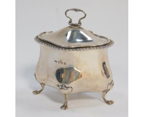 An Edwardian silver tea caddy, of bombe shaped design, with hinged lid and gadrooned flanged border, raised on four stylised 