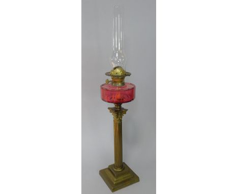 An early 20thC brass Corinthian column oil lamp, with a faceted ruby glass reservoir, with chimney, 80.5cm high.
