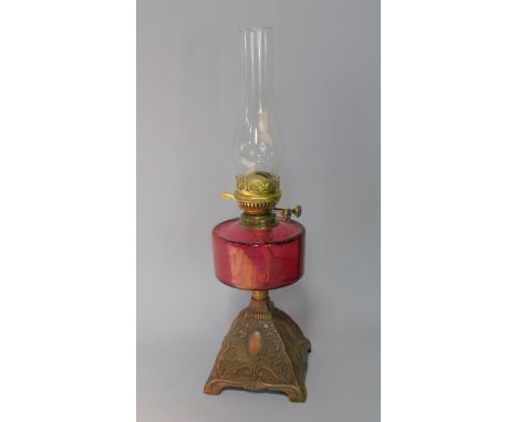 A late Victorian oil lamp, with plain cranberry glass reservoir, and double burner on a cast iron square tapered Art nouveau 