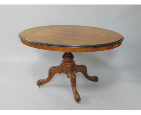 A Victorian walnut and inlaid oval tilt top loo table, raised on a foliate carved turned column and four cabriole legs on cer