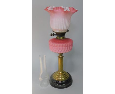 A late Victorian brass table lamp, with reeded column and black glazed red earthenware base, with pink satin moulded glass re