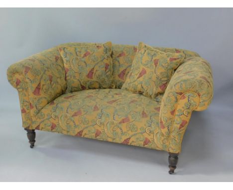 A Victorian drop arm sofa, upholstered in patterned fabric, against a fawn ground, raised on turned ebonised legs, capped on 