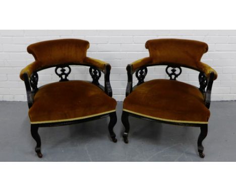 A pair of upholstered armchairs the curved back rests over a carved frieze on cabriole supports terminating on ceramic castor