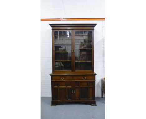 A mahogany Arts & Crafts bookcase, the moulded top above a pair of glazed doors enclosing  a shelved interior, over two friez