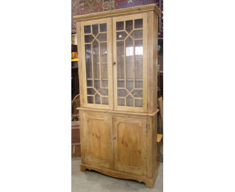 A 19th century stripped and waxed pine bookcase, the lower section enclosed by two panelled doors, the upper section by astra