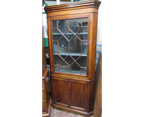 A Georgian mahogany freestanding corner cupboard, the lower section enclosed by two panelled doors, the upper section by a si