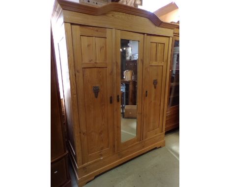 A stripped and waxed pine three door wardrobe with central mirror panel set beneath a shaped top of knockdown form for easy t