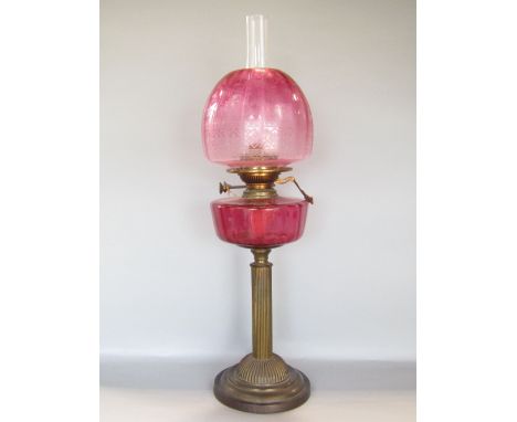 A late 19th century cast brass Corinthian column oil lamp, with cranberry glass reservoir and fluted column upon a stepped ci