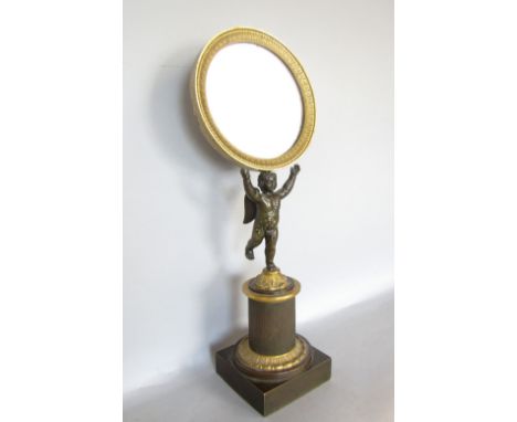 19th century bronze and gilt bronze figural mirror, the tondo glass in a darted ormolu frame, held aloft by a bronze cherub u