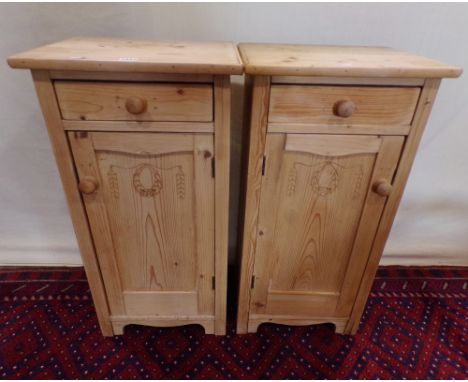 A pair of stripped pine bedside cupboards, each enclosed by a panelled door with carved detail and frieze drawer