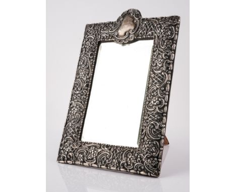 A VICTORIAN SILVER MOUNTED SHAPED RECTANGULAR STRUT BACKED MIRRORHaving floral and scroll embossed decoration and with a cart