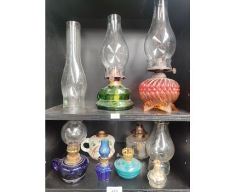 Two shelves of antique glass oil lamps and shades and shelf of brass oil lamp burners and wicks. 