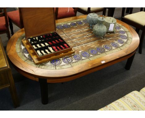 A hardwood coffee table, oval form with abstract tile decoration, on four cylinder form supports, 62 x 39in. (157.5 x 99cm.).