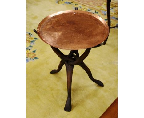 An African carved wooden tripod table with copper tray top, set on foldable interlocking stained wooden legs with animal head