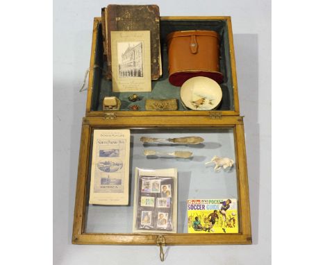 A tabletop display cabinet with hinged glass top, within which comprise a set of Binoculars, a Satsuma ceramic bowl, snakeski