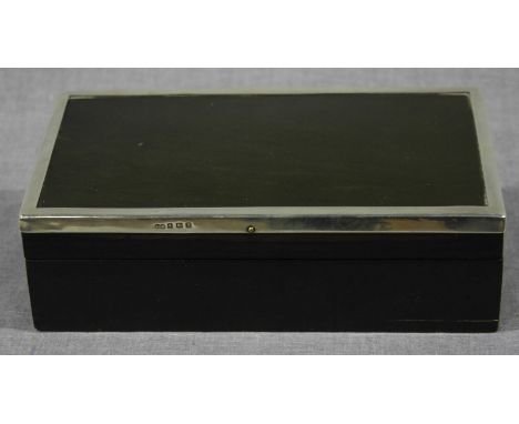 A sterling silver mounted ebony cigarette box, the hinged top opening to reveal a dual compartmented interior.