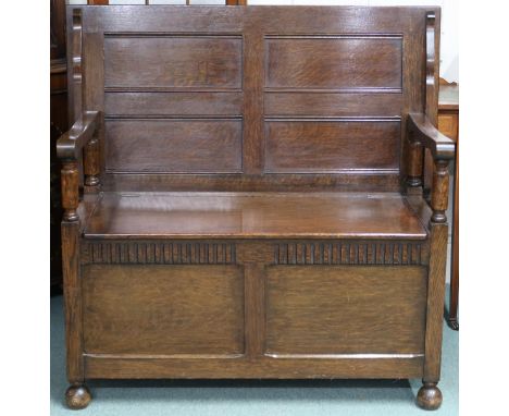 An early 20th century oak monks bench with fold-over top/back rest over hinged seat over panelled front on turned feet, 102cm