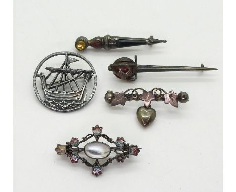 A white metal moonstone and enamel brooch in the style of Jessie M. King, a silver John Hart Viking longship brooch, two silv